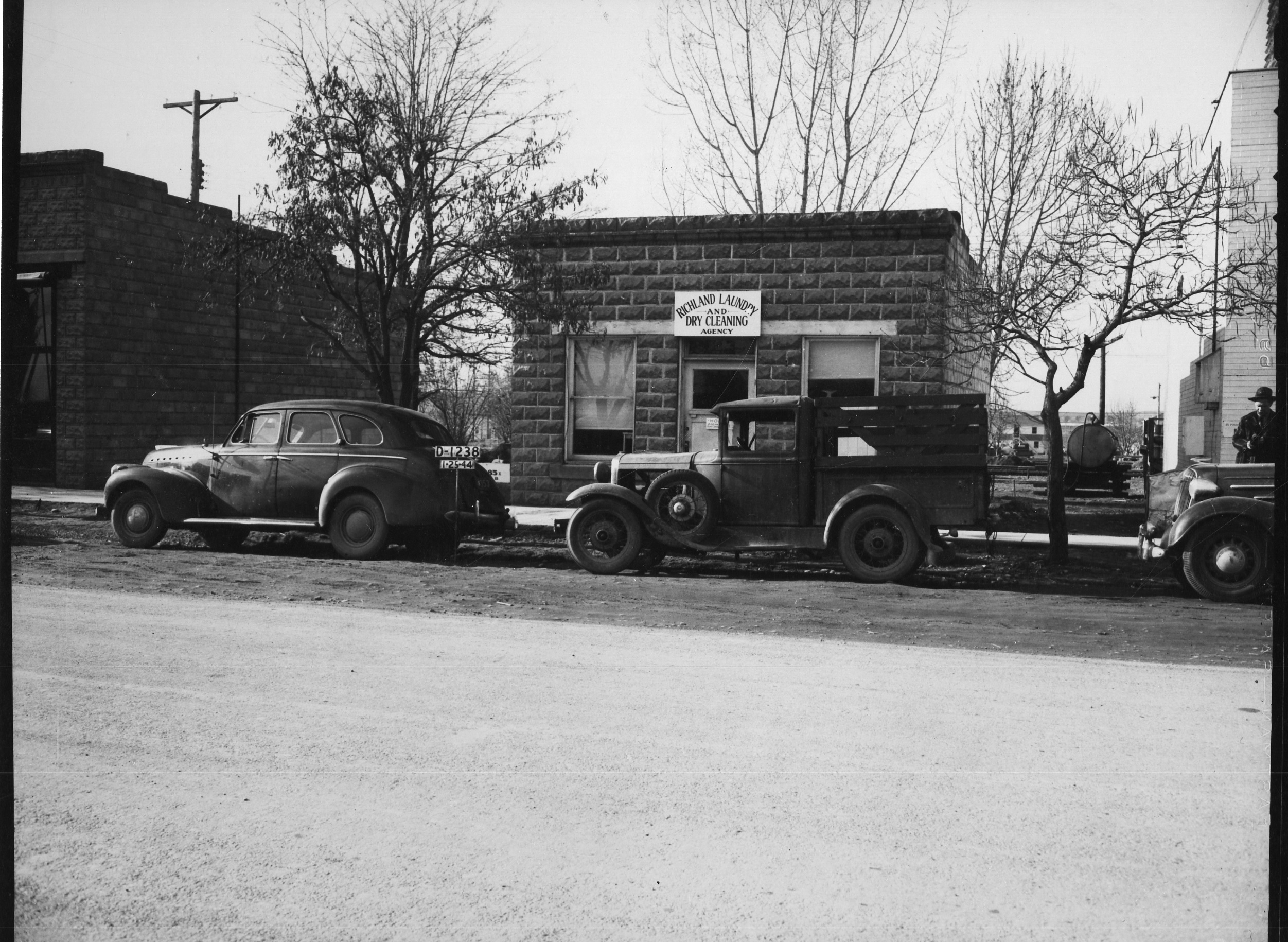 HASI.1996.001.110 Historic image of a car and truck in front of a squat one-story brick building.