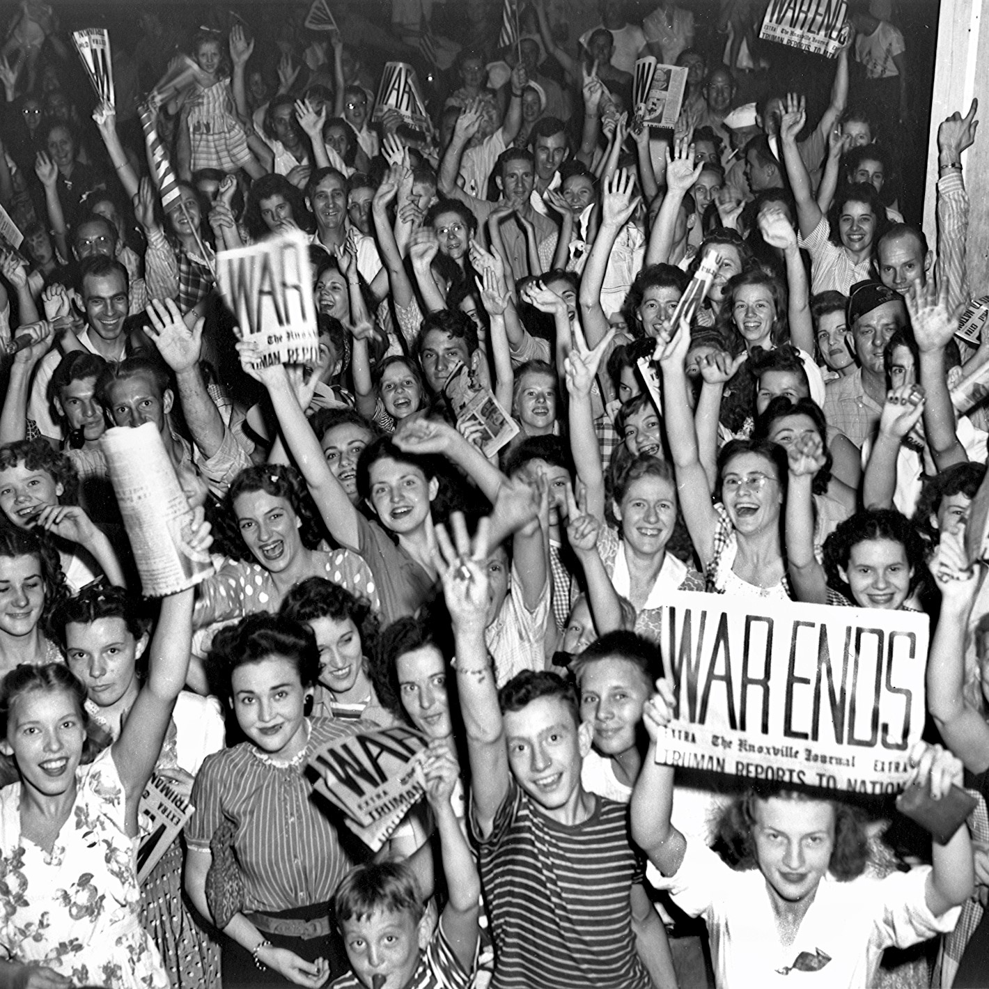 Dozens of people gather, waving and holding newspapers.
