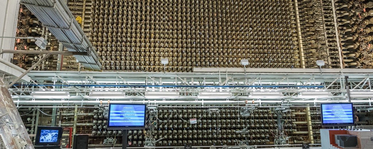 Color photo of a massive gold tinted reactor face with three tv monitors at its base.