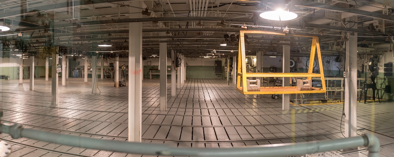 A panoramic image of a large industrial room with steel columns and a yellow cart on a pulley system.