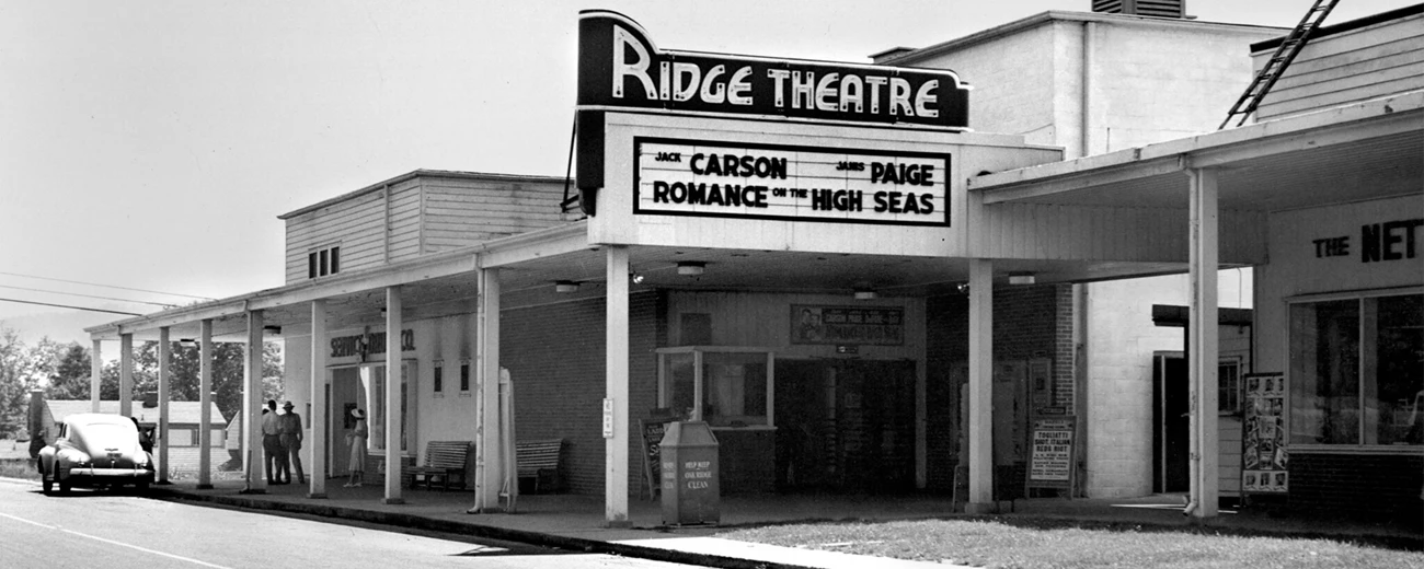 Ridge Theatre, Oak Ridge, TN A black and white photo of the Ridge Theatre with a marquee that reads “ Carson Paige, Romance on the High Seas.”