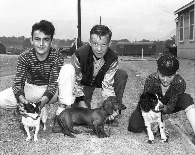 Three children kneel showing off their dogs. 
