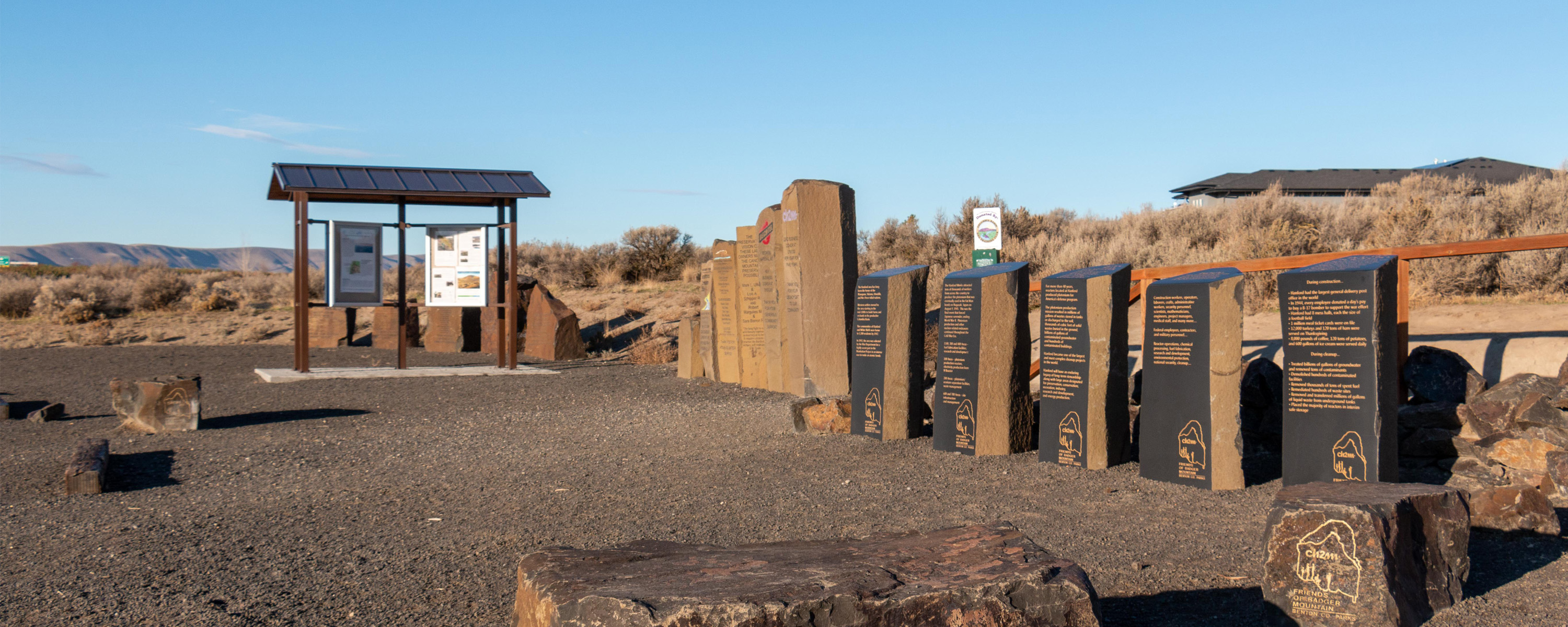 A row of large smooth rocks carved with messages on a dirt surface lead to a kiosk with signage.