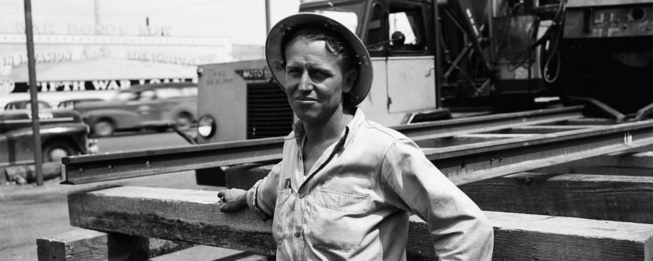 A man in a hat leans on a railing in front of a construction site.