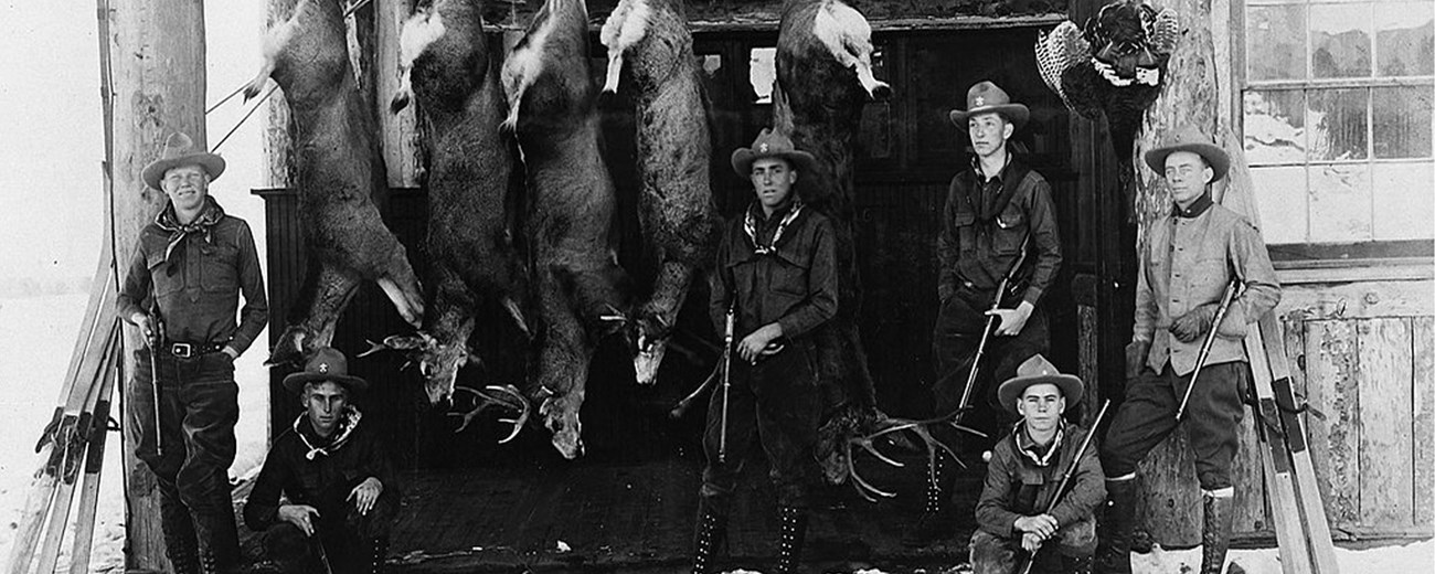 Six young men in cowboy hats pose with rifles and five dead deer.