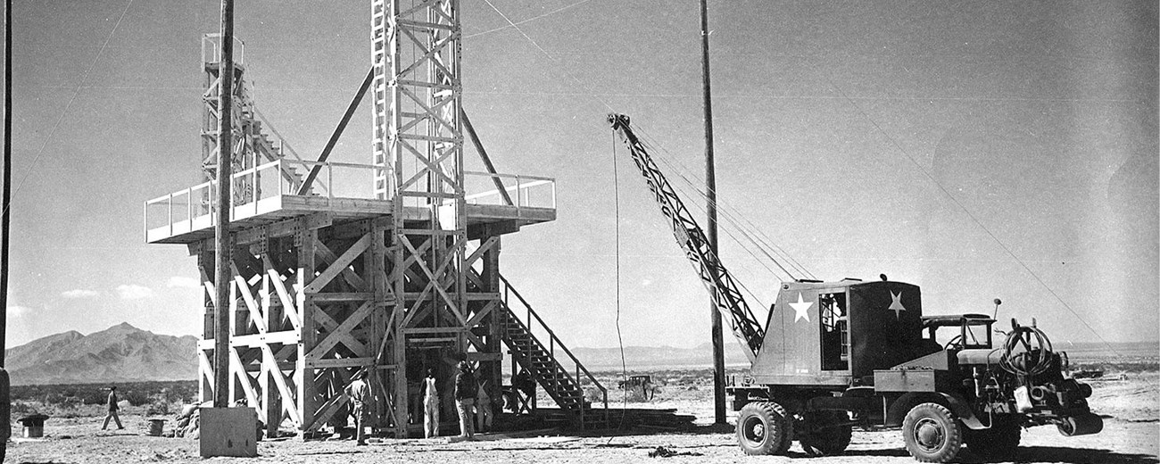 An army truck with crane attached approaches a tall man-made observation tower.