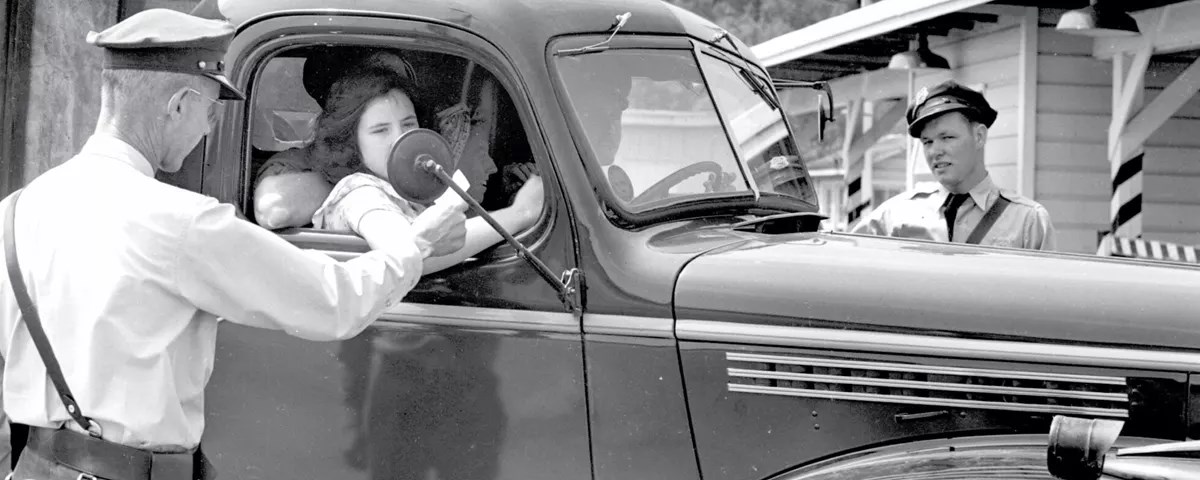 A black and white photo of a guard checking a pass of a person in a car.