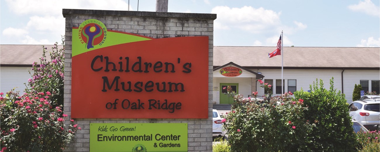 A dirty white brick sign with an orange and yellow sign that says, "Children's Museum of Oak Ridge."