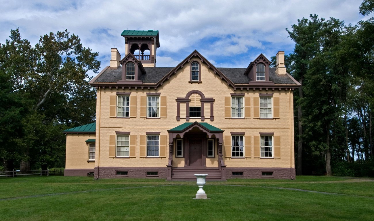 Photo of Lindenwald, a large yellow brick house, with trees and a blue sky