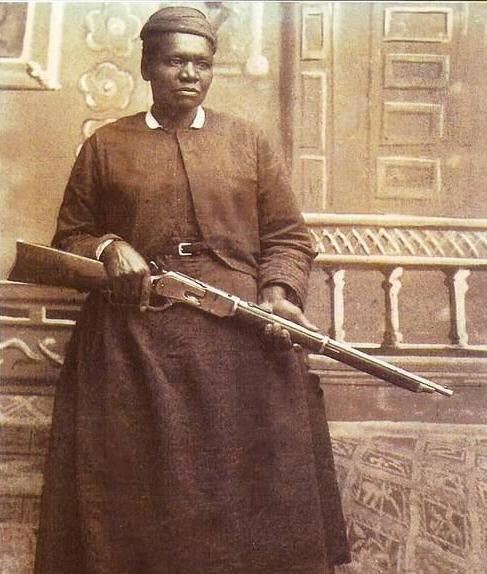 Mary Fields, in a long dress, stands with her rifle.