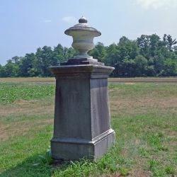 A gray granite obelisk gravesite in the middle of a field