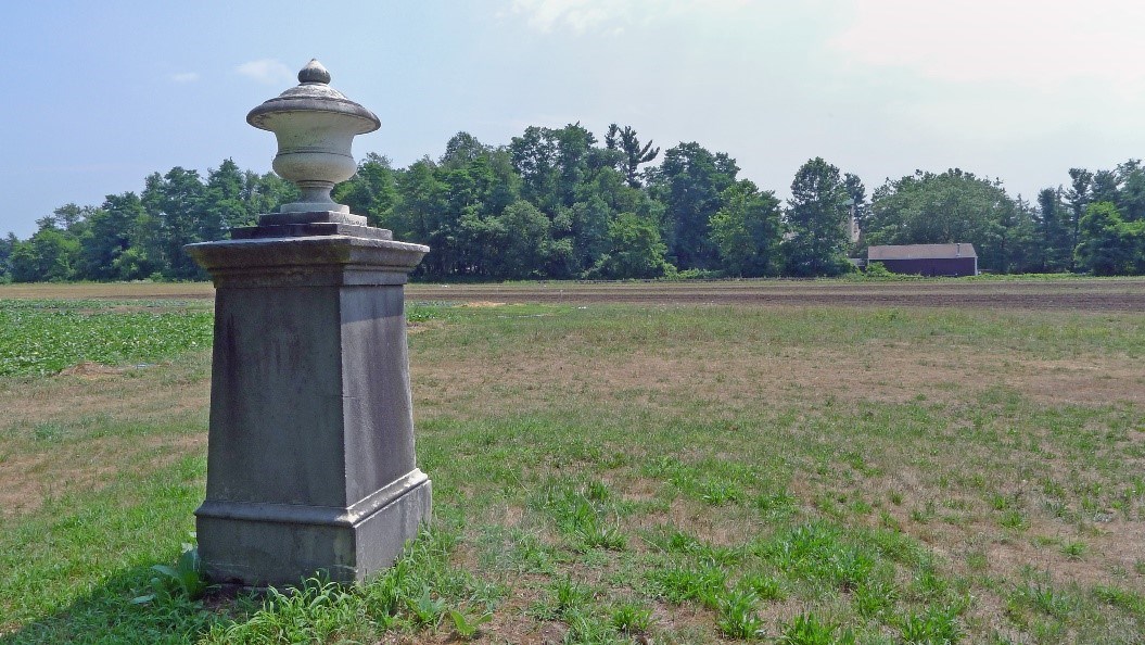 A gray granite obelisk gravesite in the middle of a field