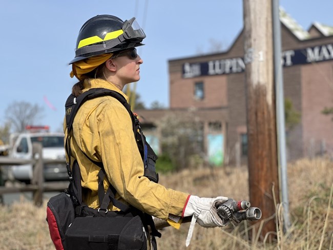 A women wildland fire worker stands at the ready.