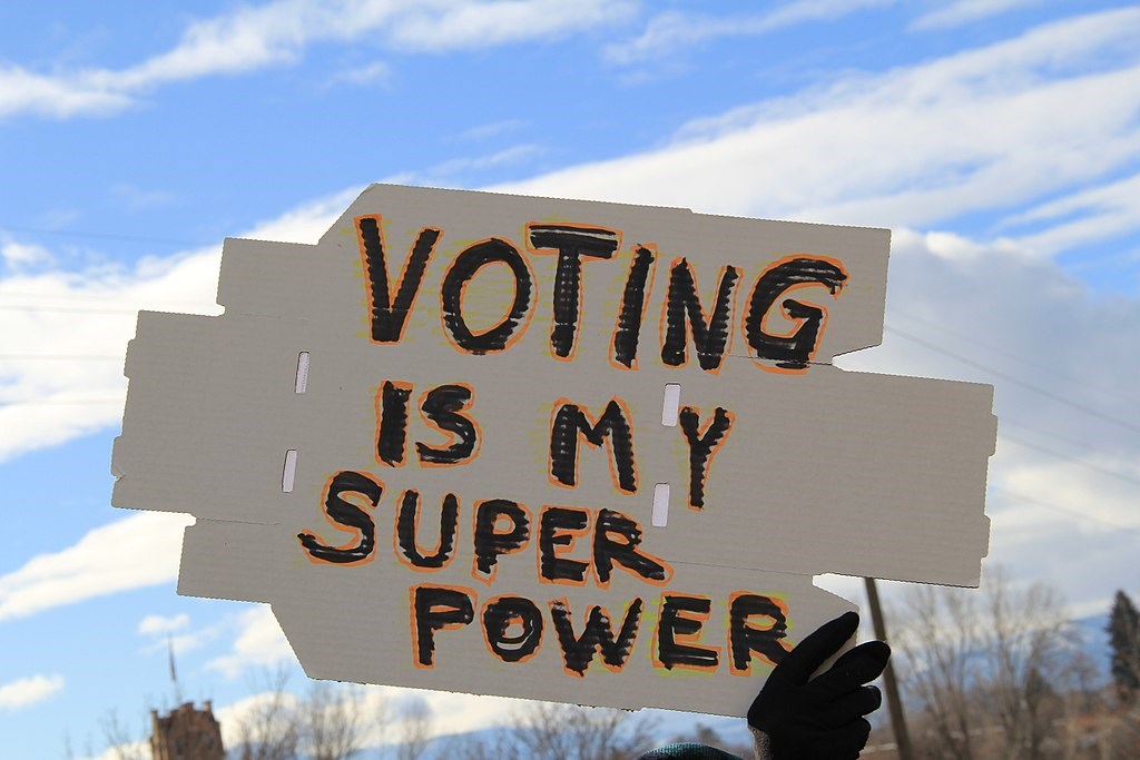 A sign reading "Voting is my Super Power" being held up against a blue sky