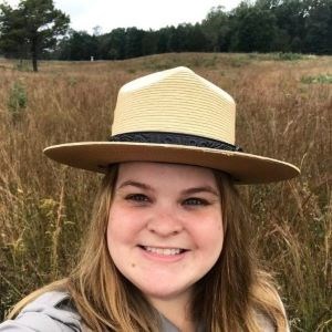 Park ranger wearing a flat hat smiling in a field