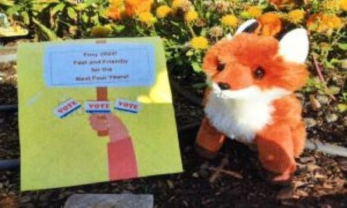 A stuffed red fox sitting in a flower bed