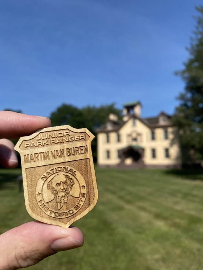 Junior Ranger badge held in front of house.