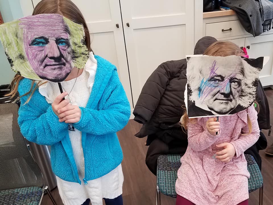 Children hold up brightly colored masks of Martin Van Buren's face