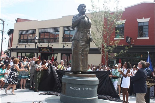 Maggie L Walker Statue Plaza A crowd is gathered outside around the unveiling of a tall, bronze statue of an African American woman