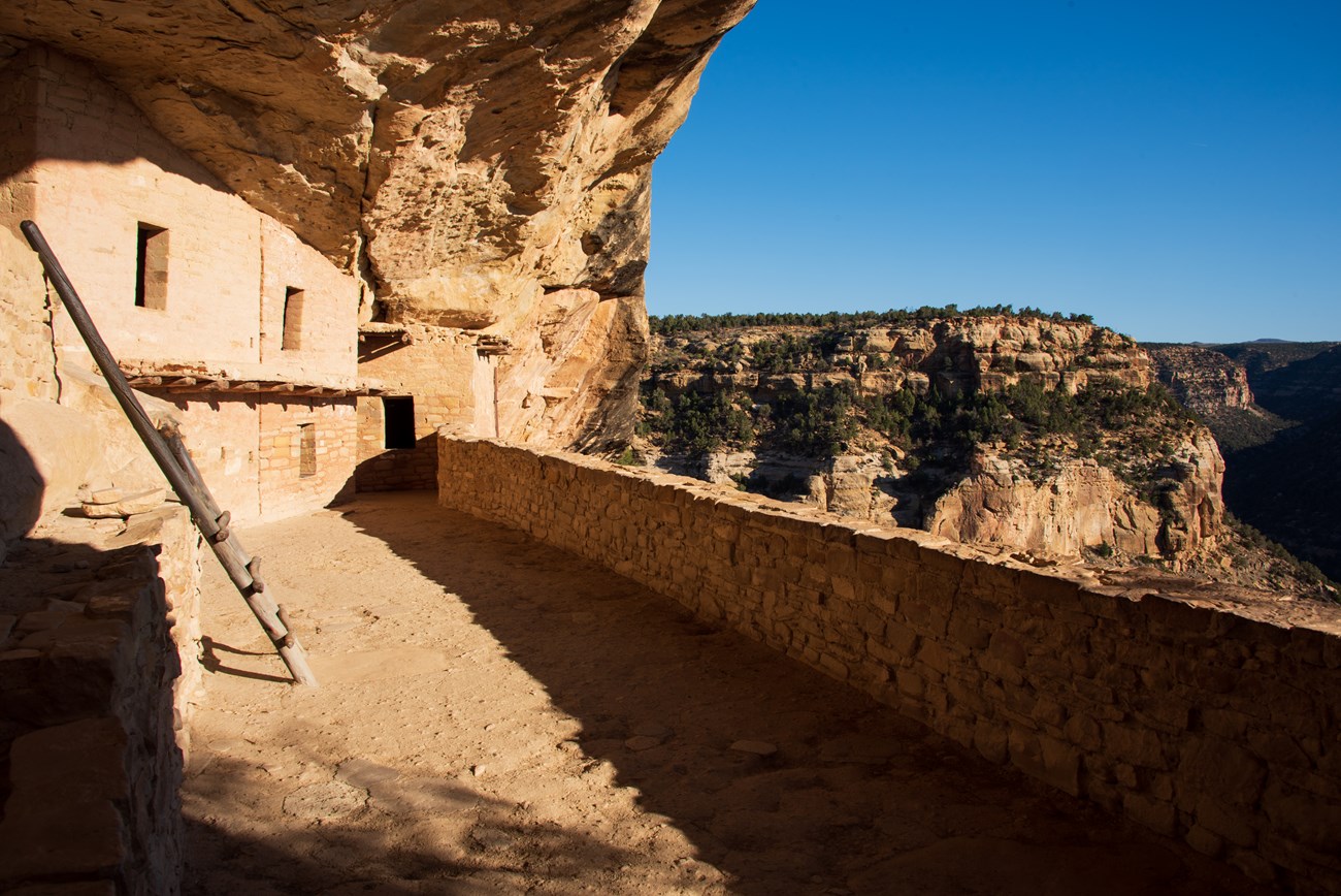 Walls of a village built of stone sits beneath a large stone overhang.