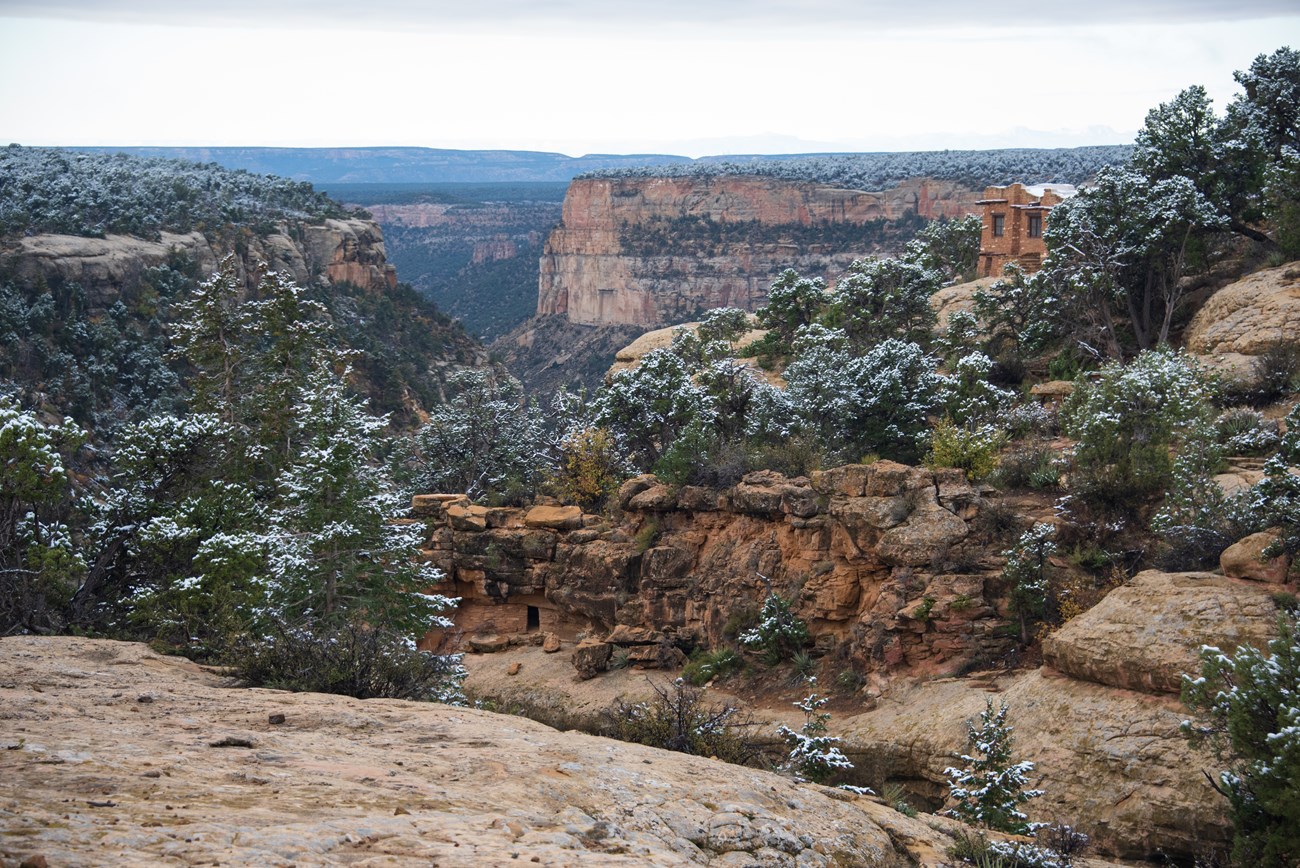 A view down a snow-covered canyon, with an ancestral site tucked in an alcove below a sandstone park building