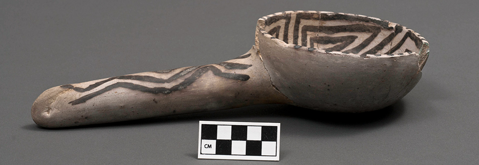 Grey pottery piece shaped like a large spoon with black painted geometric designs.