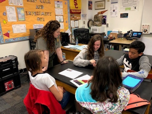A ranger is in a classroom with students seated at desks, one child has their hand raised.