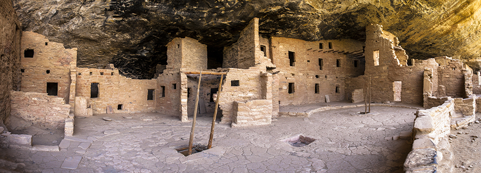 Kiva courtyard showing kiva roof, kiva entrance, and ladder with pueblo rooms in background