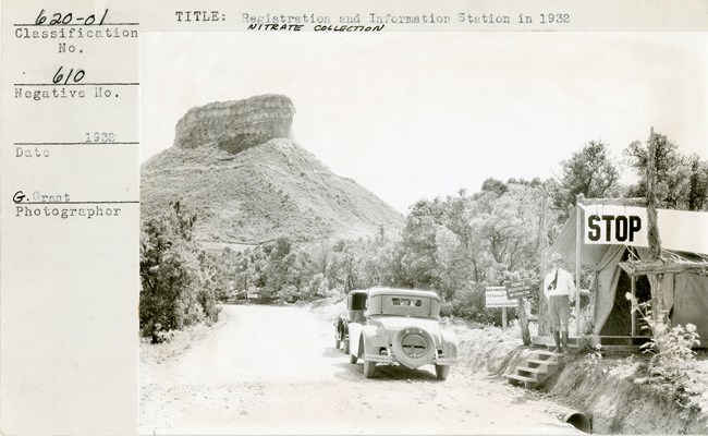 sepia tone photo 1932 car passes a ranger standing in front of an historic entrance