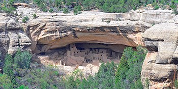 Landscape of canyon with a deeply arched-shaped space in the cliff wall. An ancient, stone-masonry village lies within its shelter.