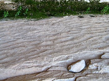 A stone's surface with a horizontal, wavy pattern eroded into it.