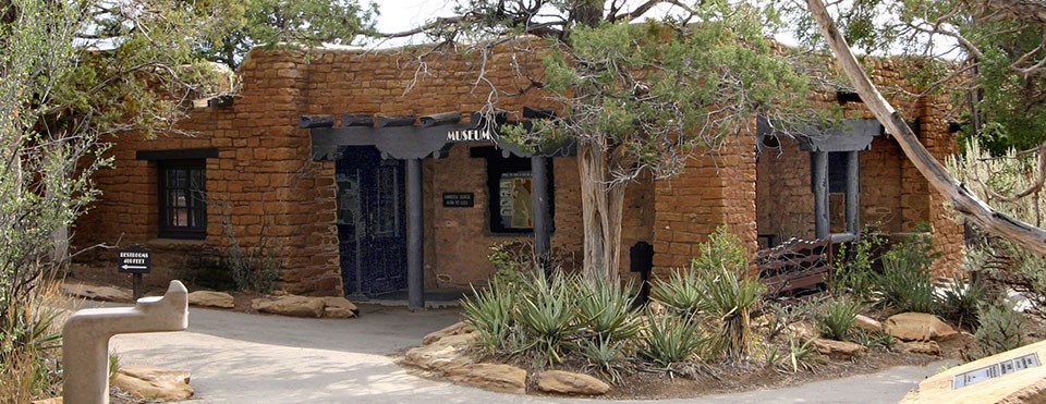 Stone, rectangular building with native plants, such as yucca in foreground.