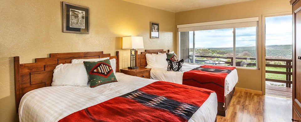 Room with two beds covered in red and black blankets. Photos hang above each bed. Window on far wall includes a door to a fenced balcony.