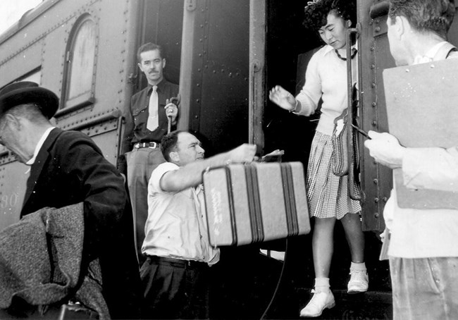 Woman stepping off train and man handing her luggage