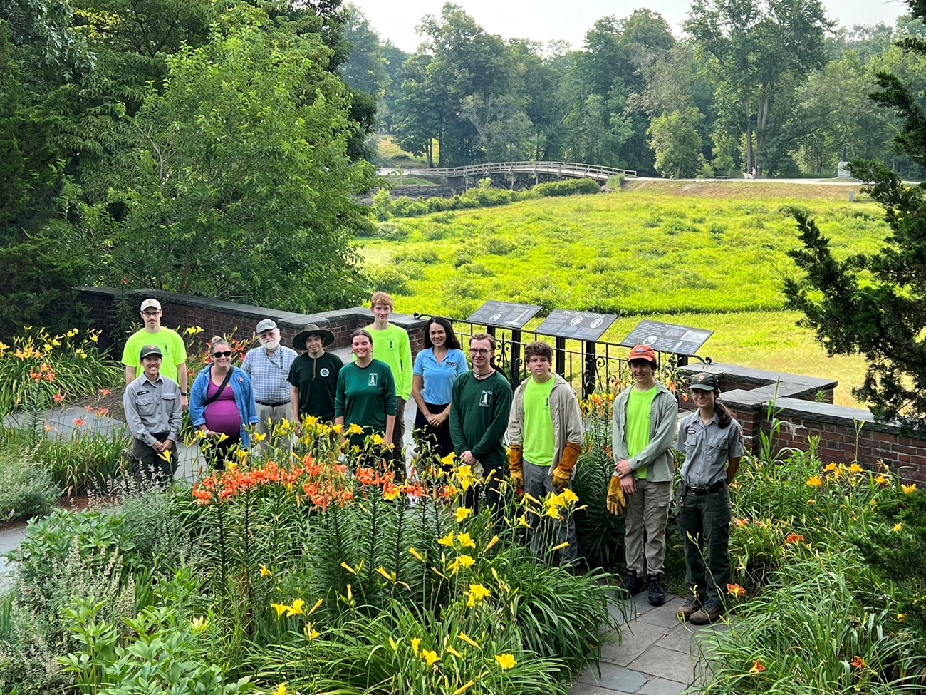Twelve interns and park employees stand in the Buttrick gardens, the North Bridge is in the background.