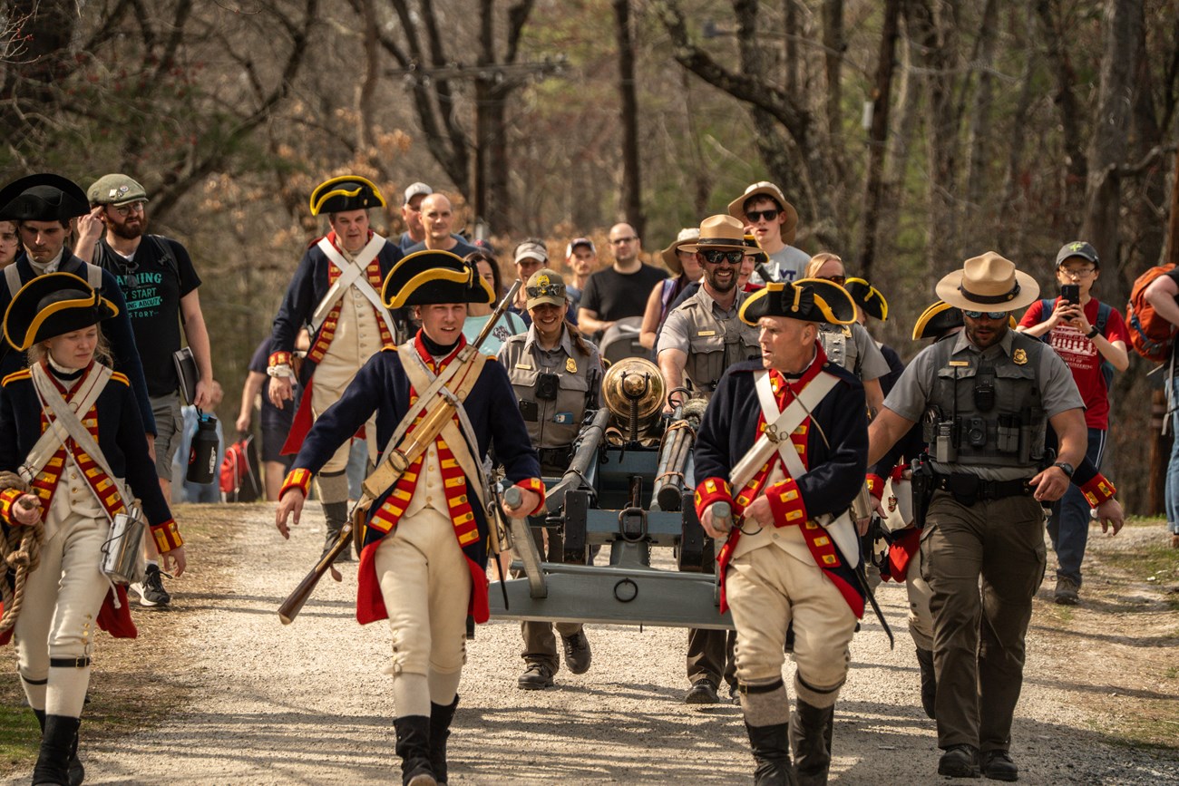 A group of park rangers and volunteers in royal artillery unfiroms pull a cannon down a road