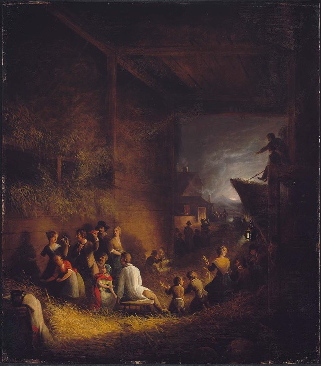 A painting of couples gathered together in a large barn filled with hay. The couples are working to husk corn collected on the floor in large heaps. One young man is holding a red ear of corn appears to ask for a kiss from a nearby woman.
