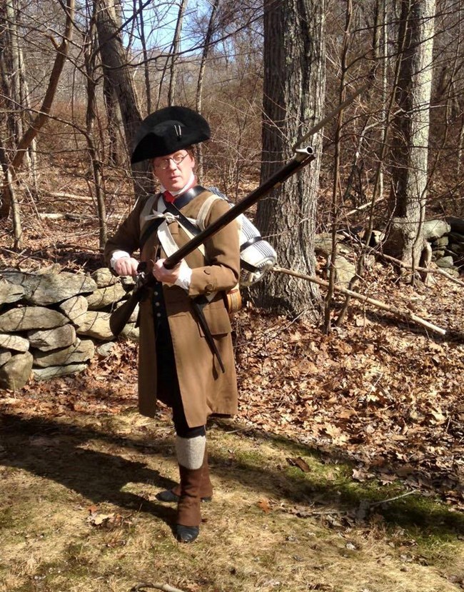 Man dressed as a Revolutionary War soldier with a brown coat, musket and bayonet