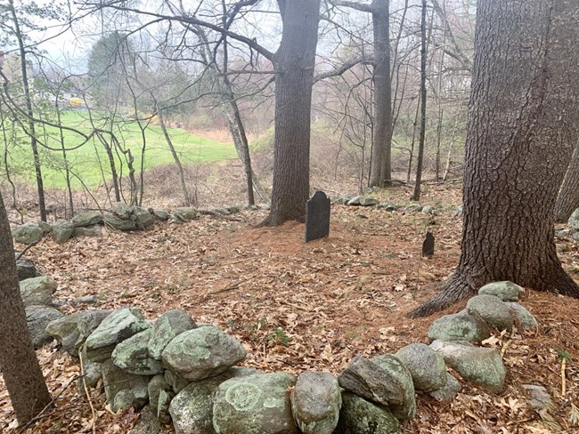 The headstone and footstone marking James Chandler’s grave stand in the center of a small burial plot surrounded by stonewalls and large trees.