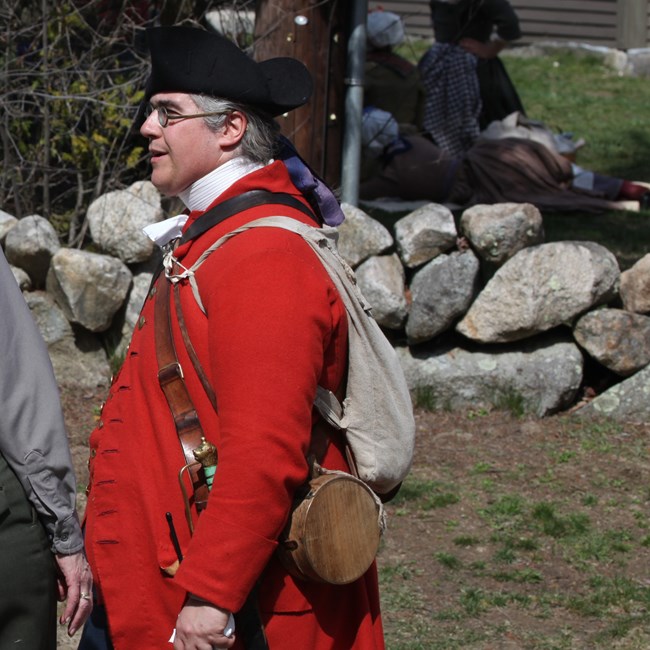Man dressed as a Revolutionary War soldier with a red coat and black hat, fancy sword and knapsack.