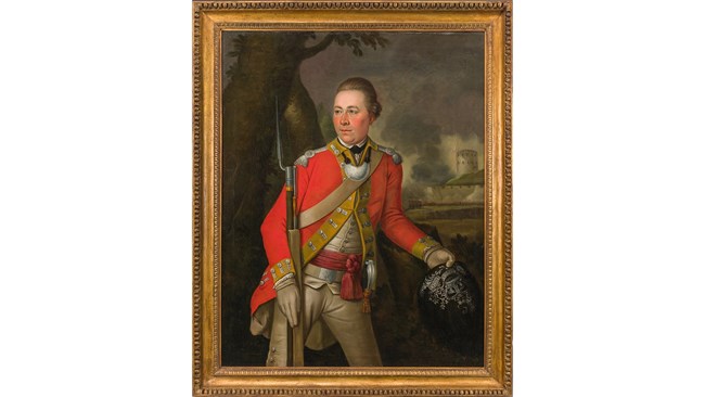 British officer with red coat with yellow trim armed with a musket and holding a black fur cap