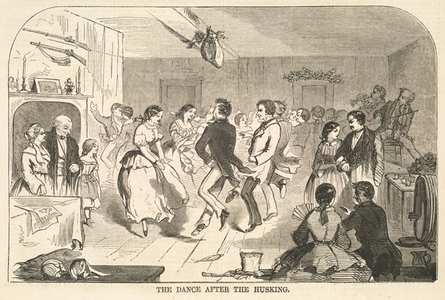 Many couples dancing within a Victorian style home. In the back right corner of the room a band is playing while other couples sit along the edges watching the dancers. Near a fireplace on the right side an older couple stands watching with a young girl.
