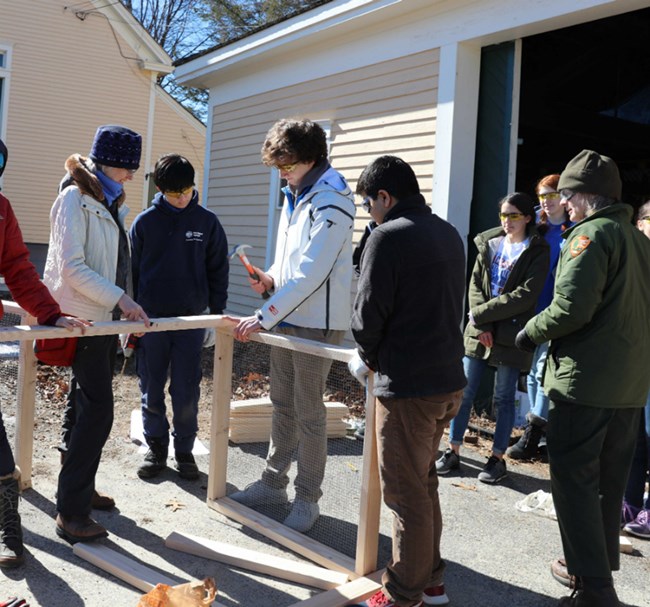 student with hammer nails wood together for compost bin