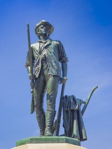 A bronze statue of a man dressed in colonial clothing carrying a musket. the man is stepping away from a field plow.