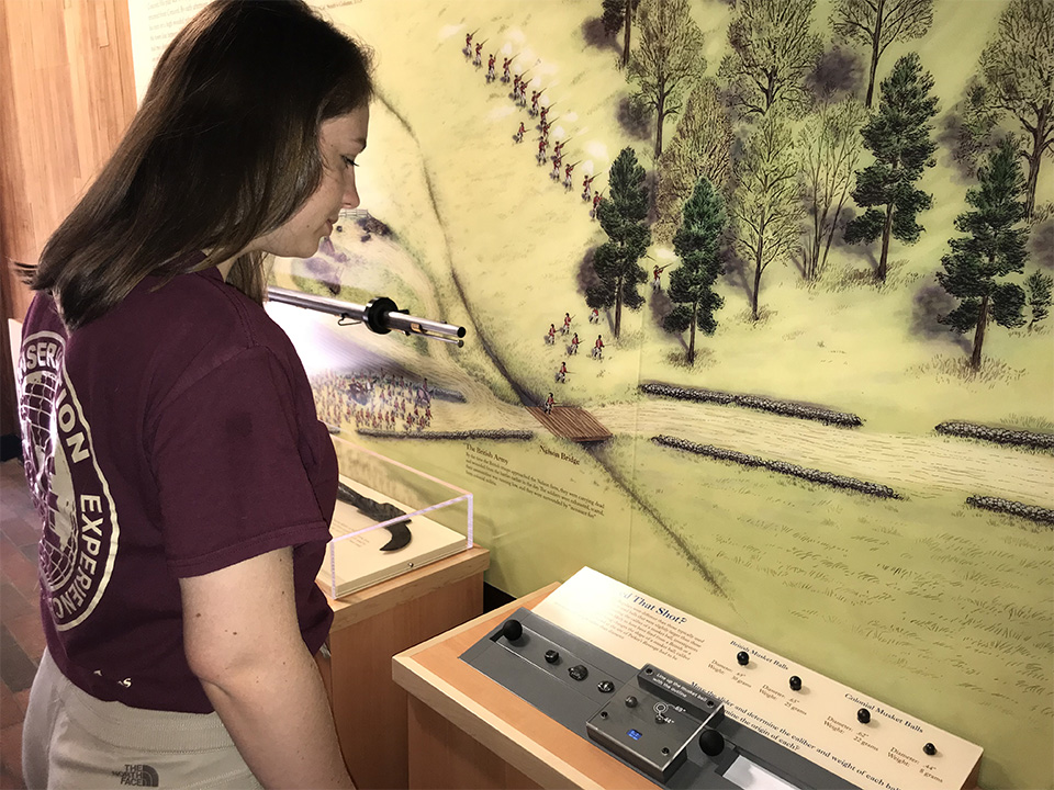 Young woman in a maroon t-shirt looks at new exhibit at Minute Man Visitor Center New Exhibit at Minute Man Visitor Center