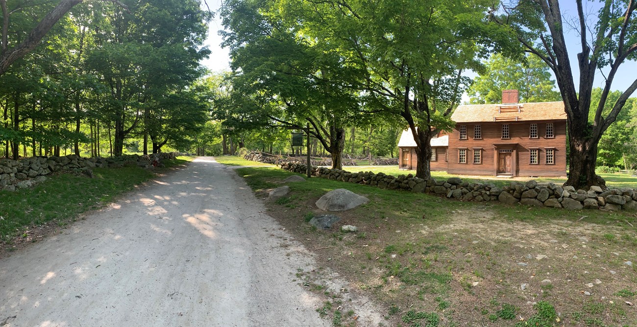 A long road flanked by stone walls passes an 18th century wooden house