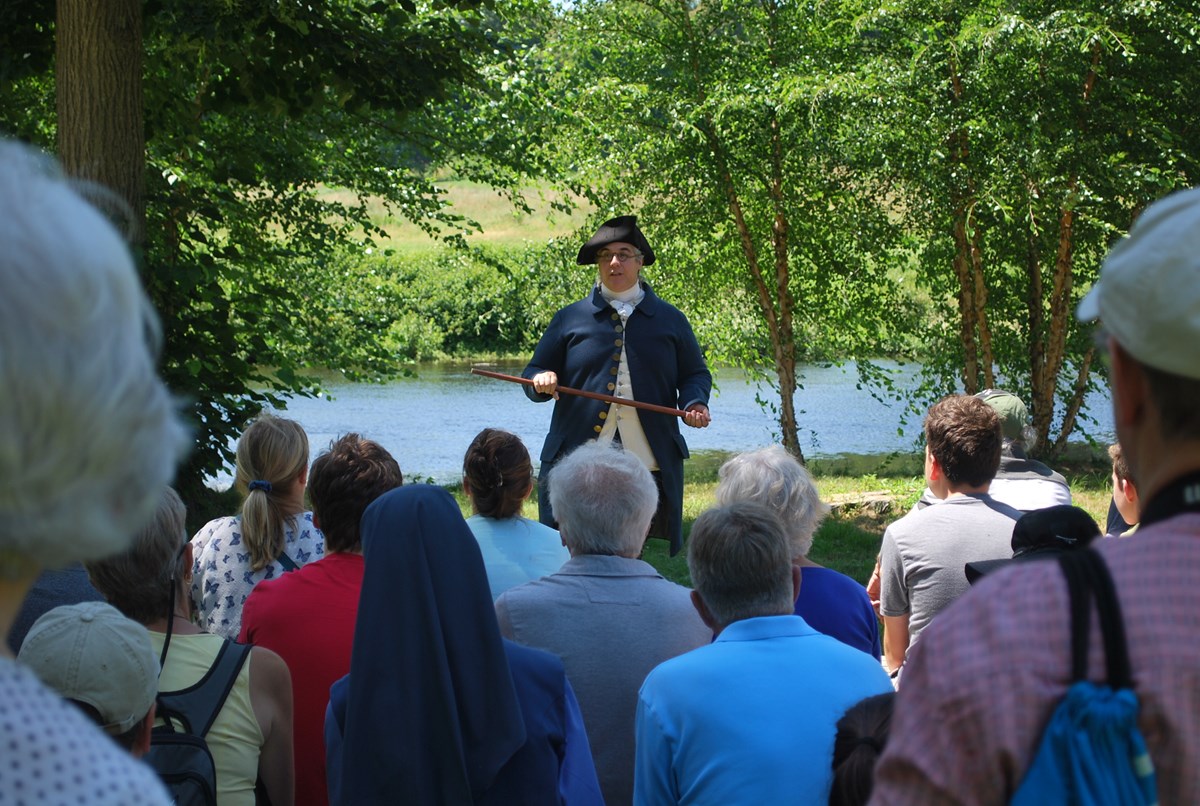 A park ranger in colonial clothing talks to a large group of visitors