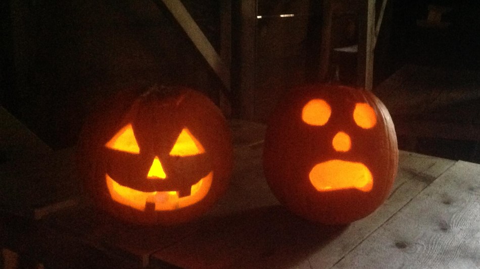 Two carved and lit orange jack-o-lanterns set on a rustic, wooden surface.