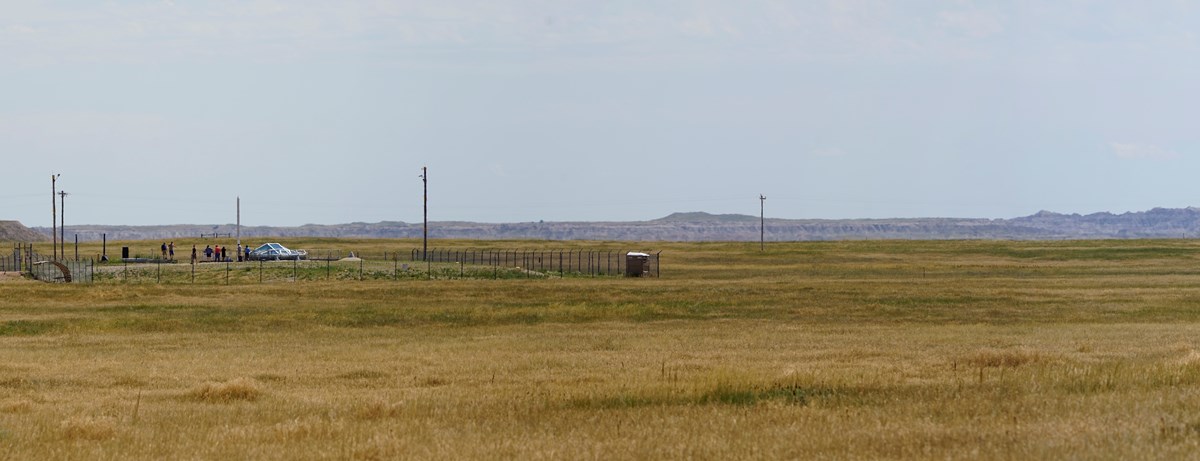 A fenced enclosure with concrete and metal features is surrounded by a prairie landscape