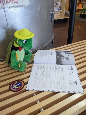 Plush turtle character sitting on bench looking at book